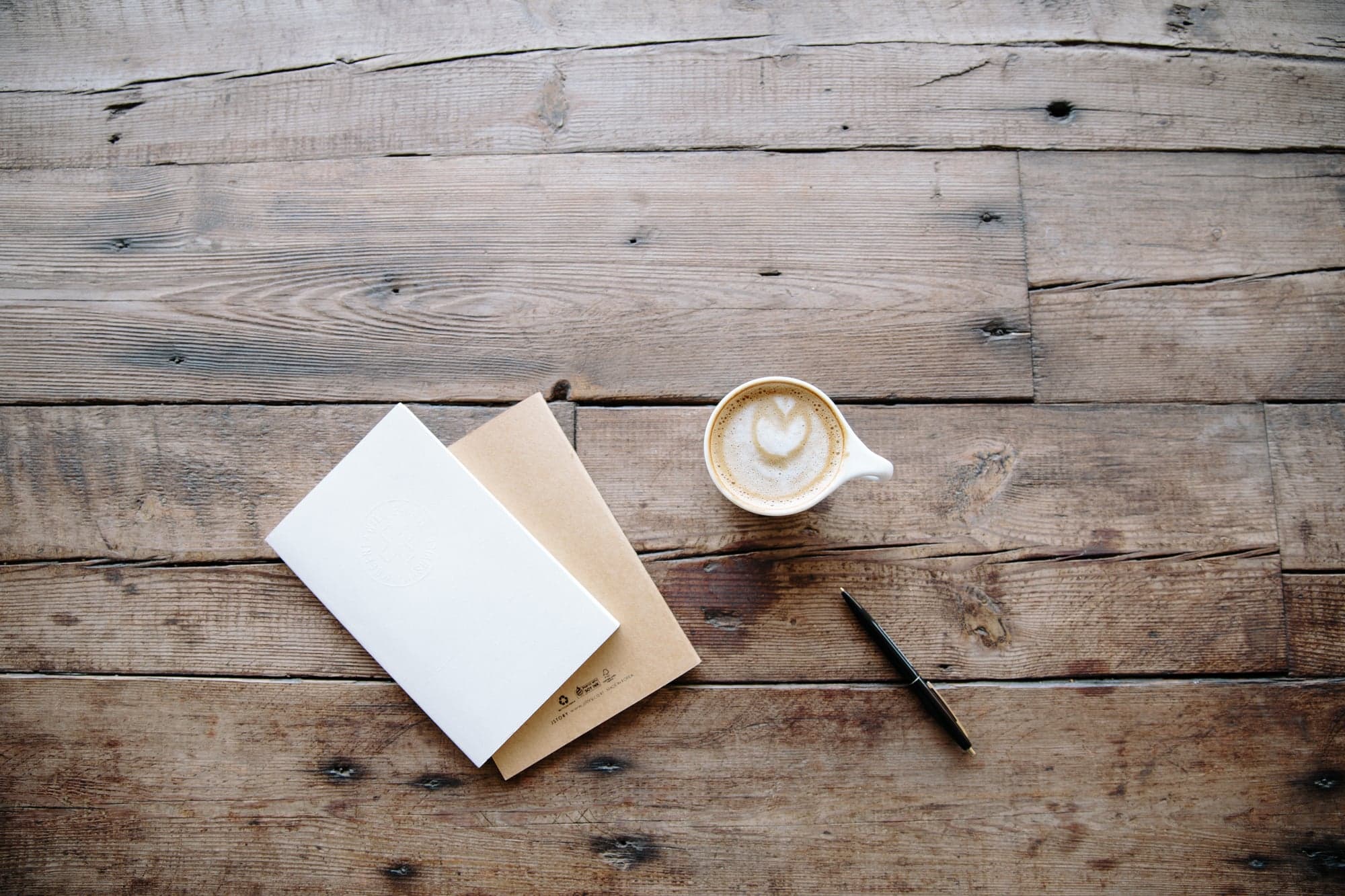 A notebook, pen, and coffee on a wooden desk